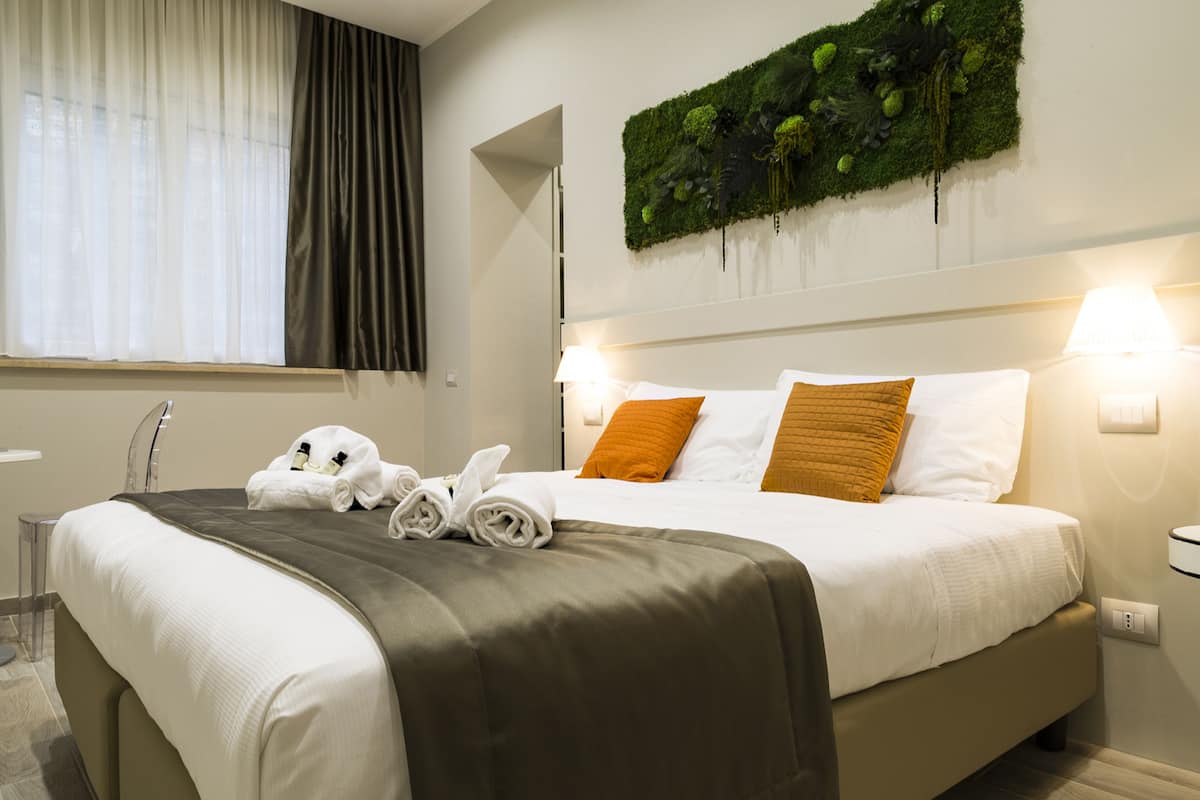 Une chambre d’hôtel avec un lit bien fait, une décoration murale verte et une fenêtre avec des rideaux.