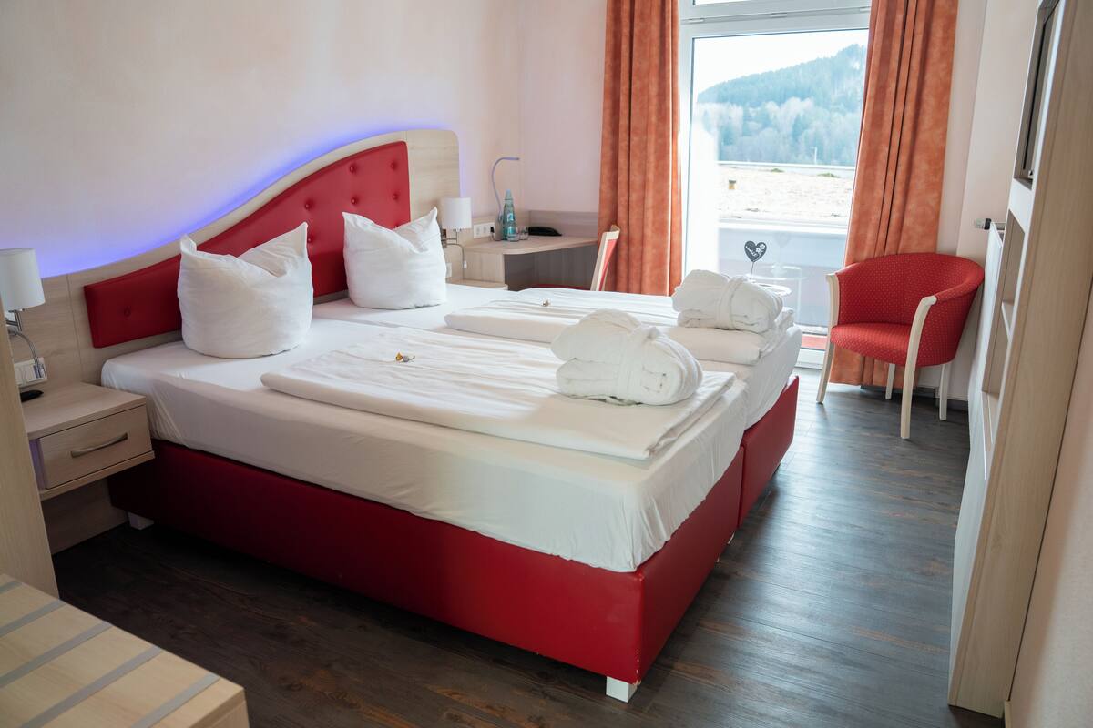 A hotel room with a large bed, a red headboard, white bedding, and a view of the outdoors.