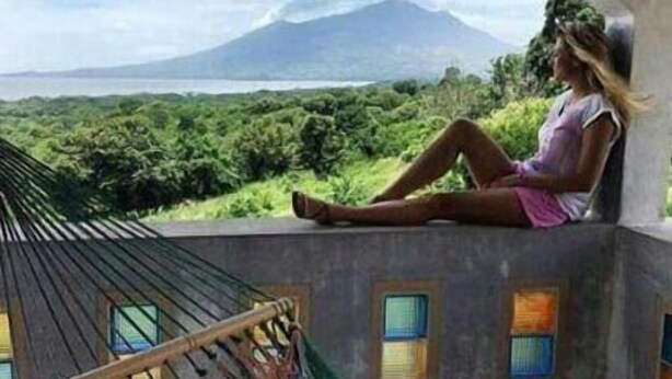 Eine Frau sitzt auf einem Balkon mit Blick auf einen Berg und das Meer.