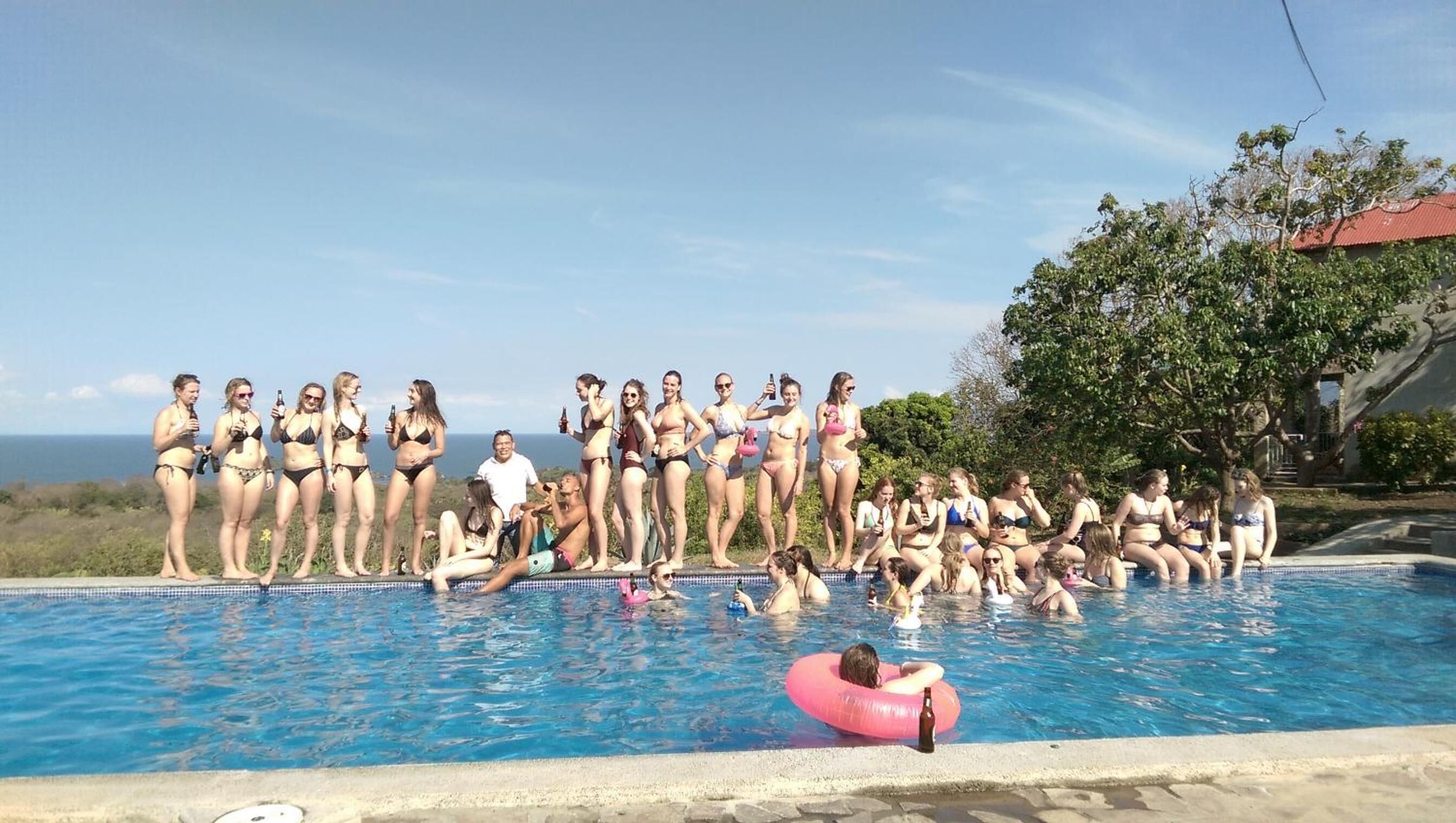 A group of people in swimwear by a pool with a view of the ocean.