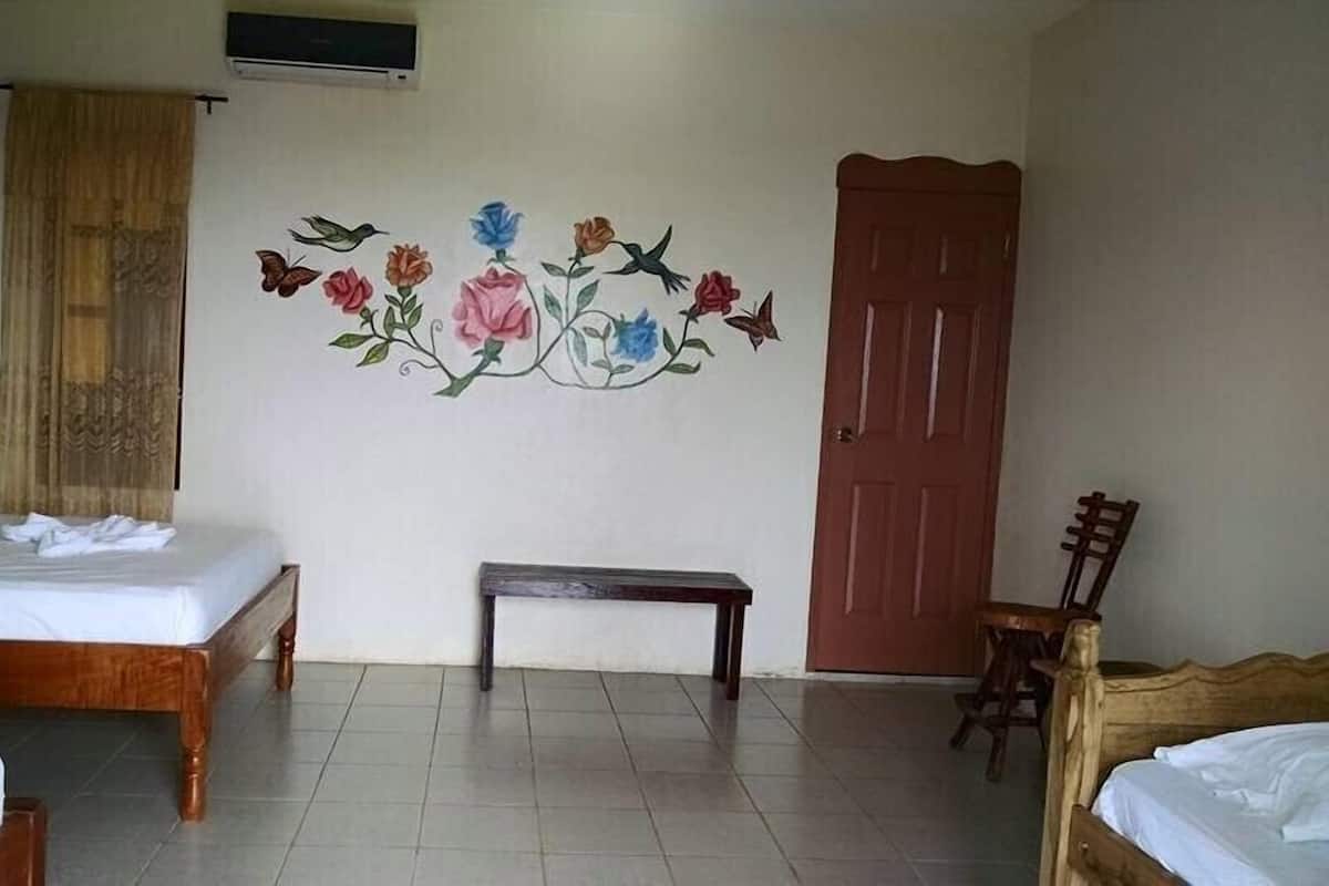 Ein Hotelzimmer mit zwei Holzbetten, einer Bank, einem Holzstuhl, einer Tür und einer Wand mit floralen und Vogelmotiven.