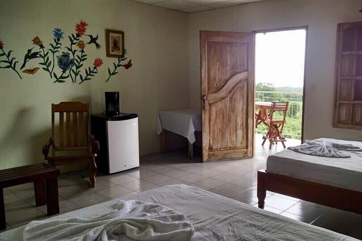 Ein Zimmer mit zwei Betten, einem kleinen Tisch, einem Stuhl, einer Kaffeemaschine und einer Wand mit floralen Verzierungen.