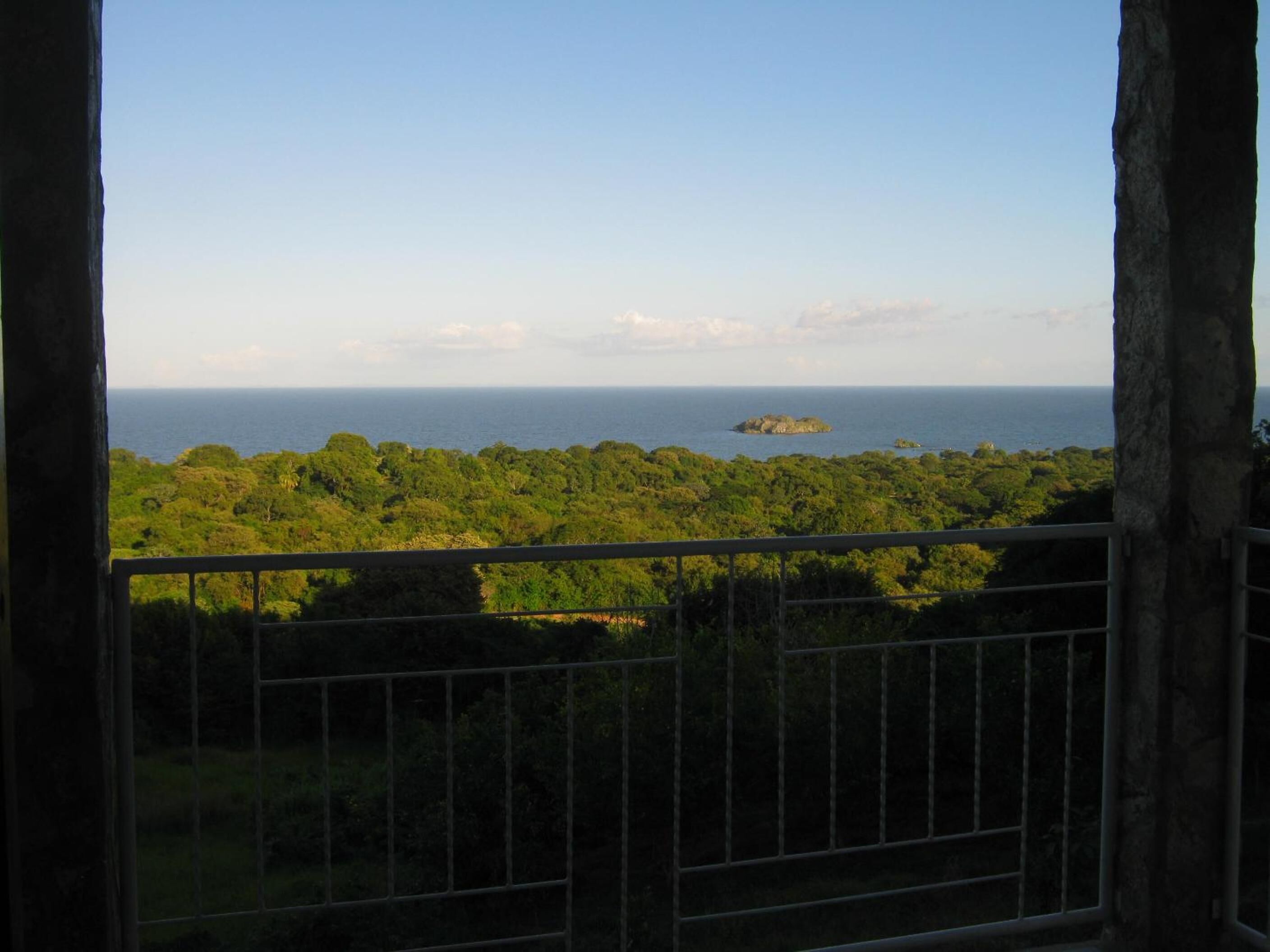 Vista des d'un balcó amb barana, sobre un paisatge verd i exuberant i una petita illa a la distància.