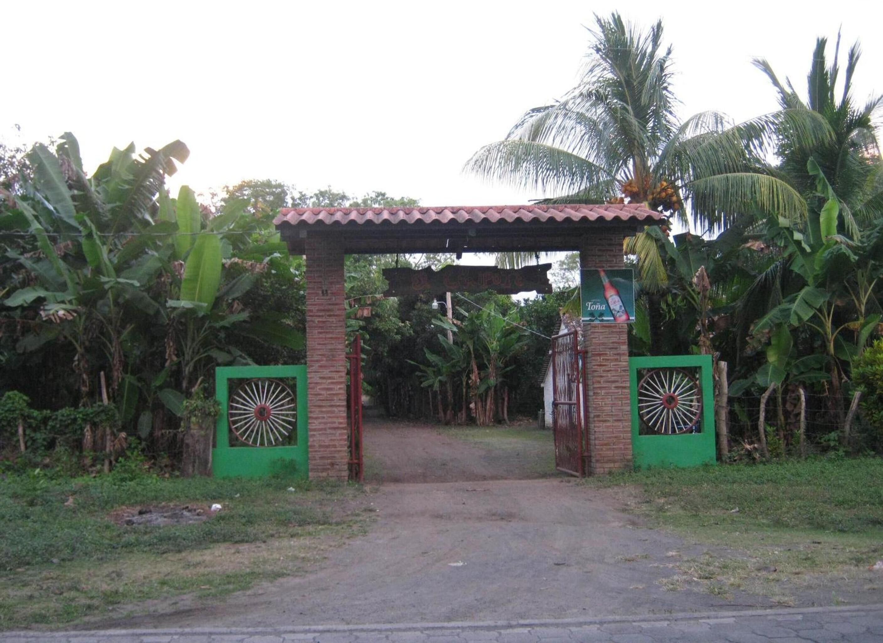 Una entrada protegida por un arco de ladrillo y techo de tejas, rodeada de abundante vegetación y palmeras.