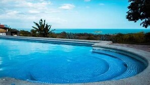 Ein Pool mit geschwungener Kante, umgeben von einem Kiesstrand und tropischer Vegetation.