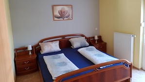 A bedroom with a wooden bed, two bedside tables, a nightstand, a radiator, and a wall-mounted picture. - Albergo Restaurante Da Franco (Buechenbeuren)
