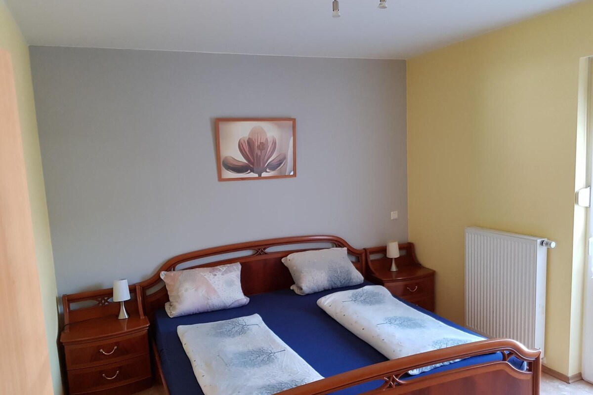 A bedroom with a wooden bed, two bedside tables, a nightstand, a radiator, and a wall-mounted picture.