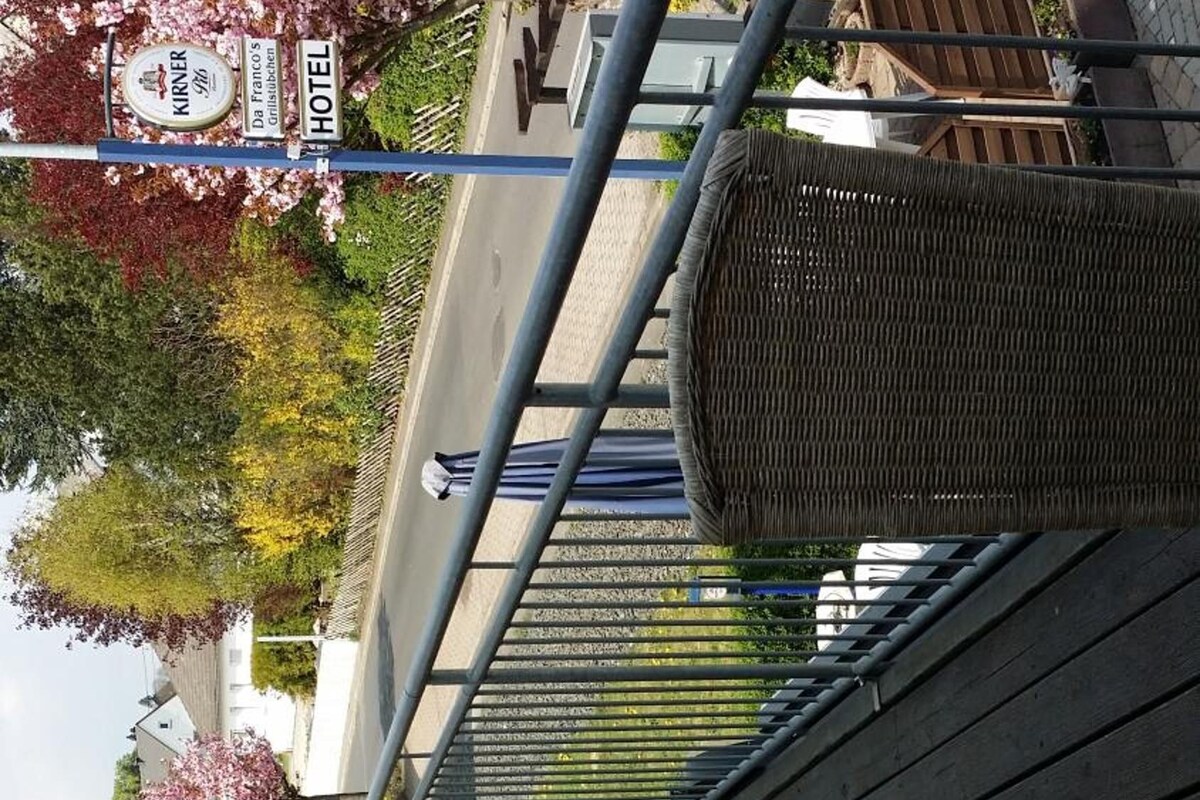 An outdoor seating area with wicker chairs and a metal railing, overlooking a street with a hotel sign.