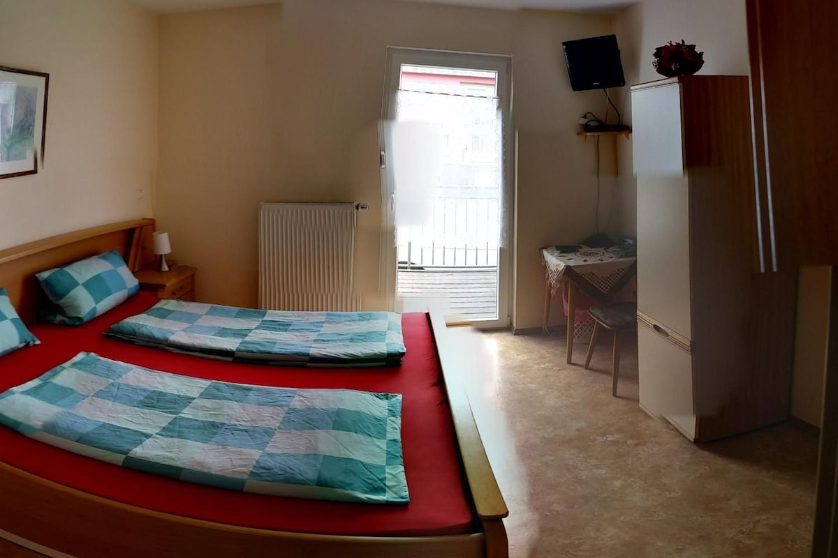 A hotel room with a bed, a desk, a chair, and a radiator.