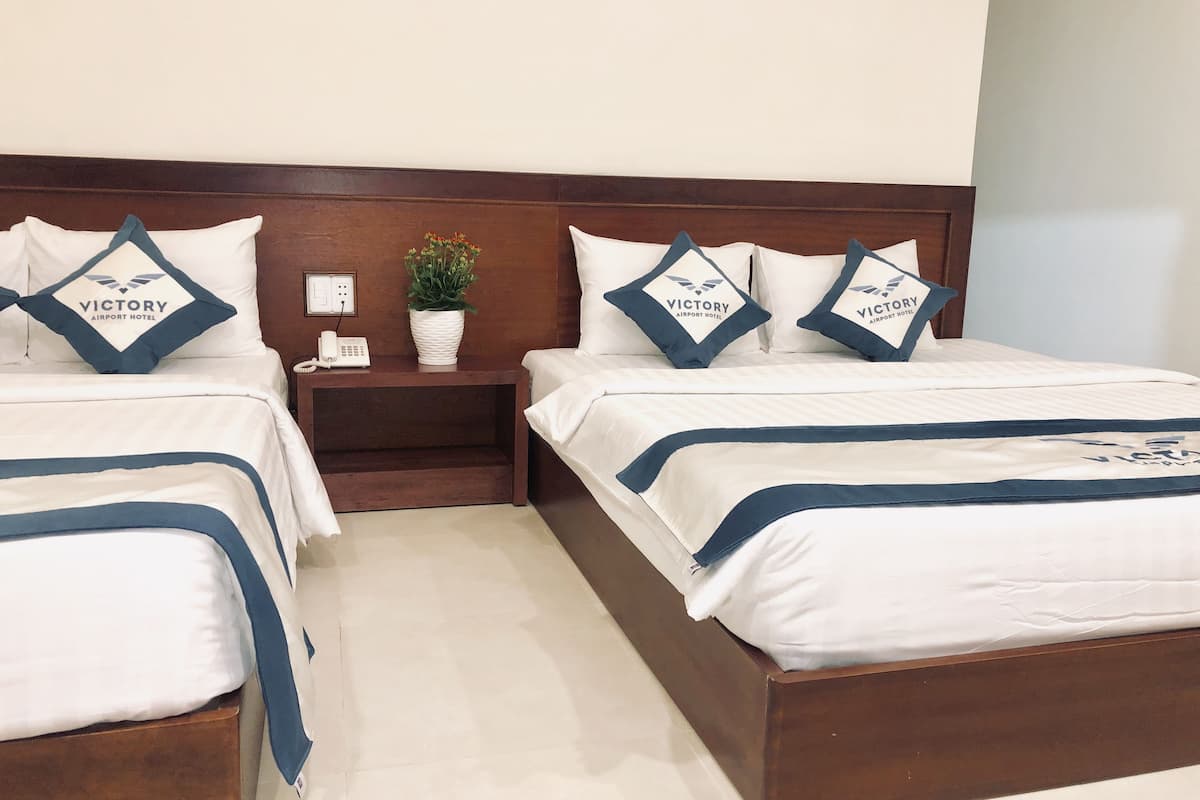 A hotel room with two beds, each with a matching headboard and pillow, a bedside table with a phone, and a small potted plant.