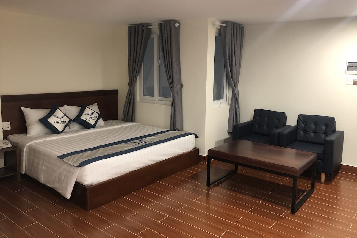 A hotel room with a bed, a nightstand, a desk, a chair, and a window with curtains.