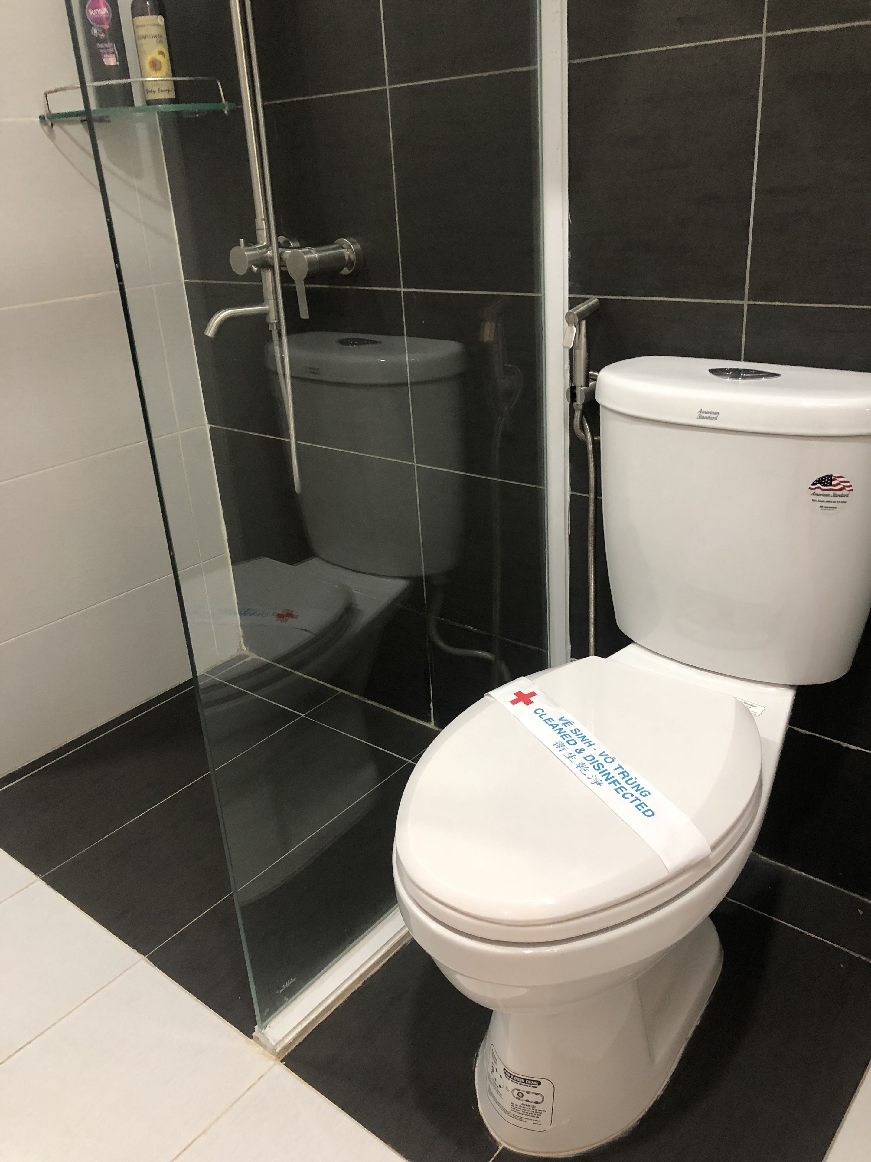 A modern bathroom with a white toilet, a glass shower enclosure, and black tiled walls.