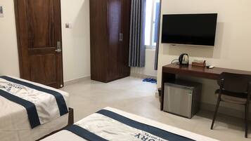 A hotel room with two beds, a desk with a TV, a wardrobe, and a small fridge.