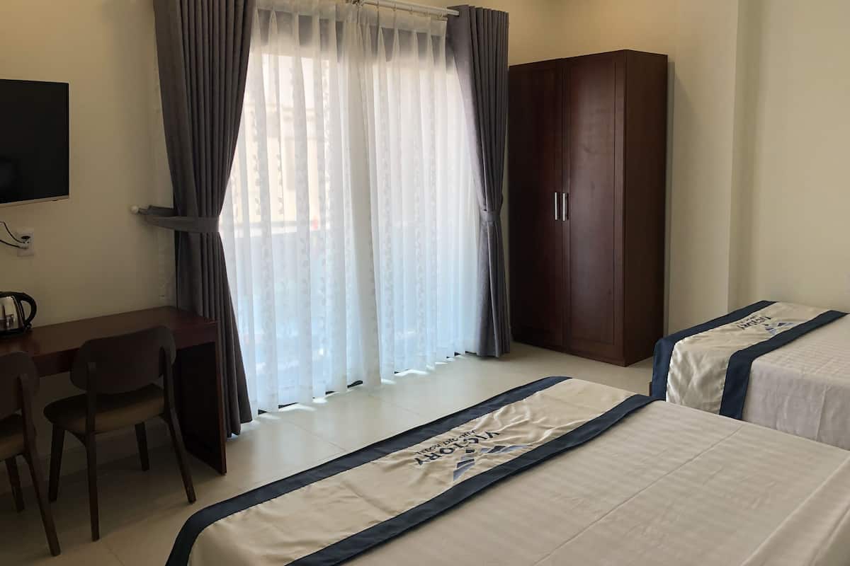 A hotel room with two beds, a desk, a chair, a wardrobe, and a TV.