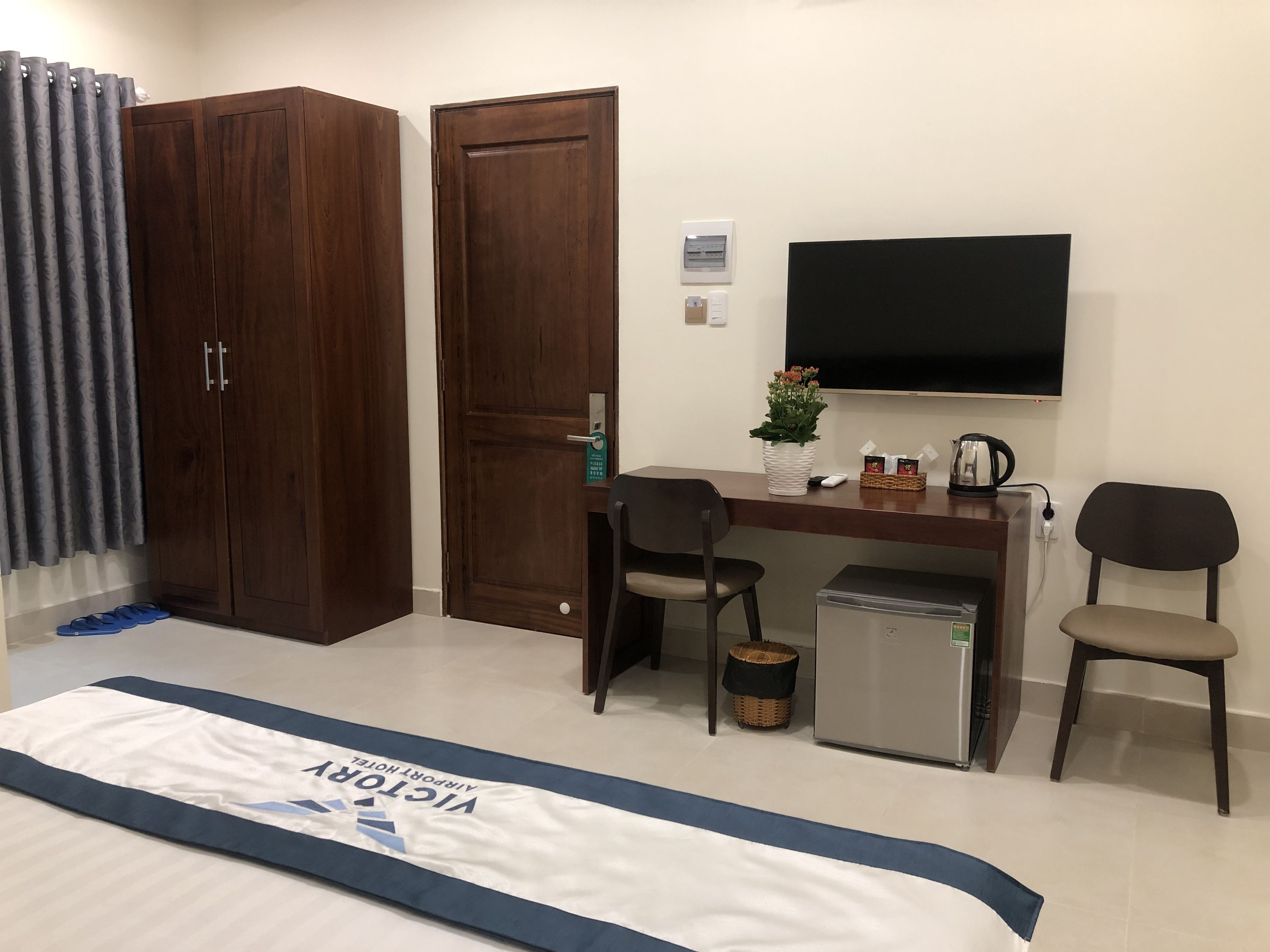A hotel room with a bed, a desk with a chair, a television, and a small refrigerator.