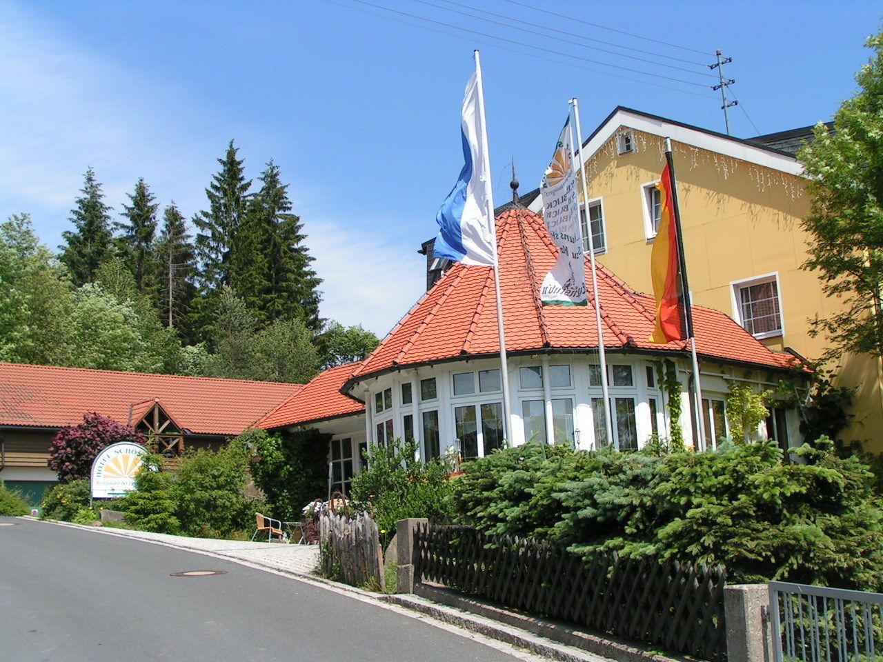 A building with a red-tiled roof, multiple flags, and a sign that reads "Hotel Schlosser."