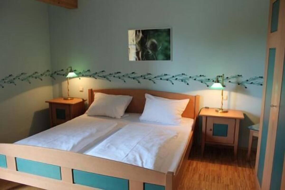 Une chambre à coucher avec un lit en bois, deux tables de chevet avec des lampes, un tableau accroché au mur et une guirlande décorative.