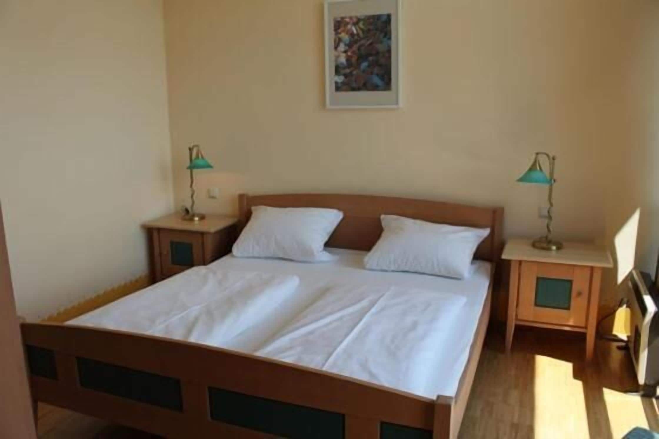 A single bed with a wooden frame and white bedding, two bedside tables with lamps, and a framed picture on the wall.