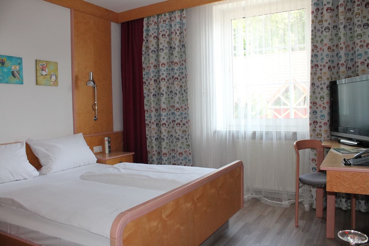 Une chambre d’hôtel comprenant un lit, un bureau avec une chaise, une télévision et une fenêtre avec des rideaux.