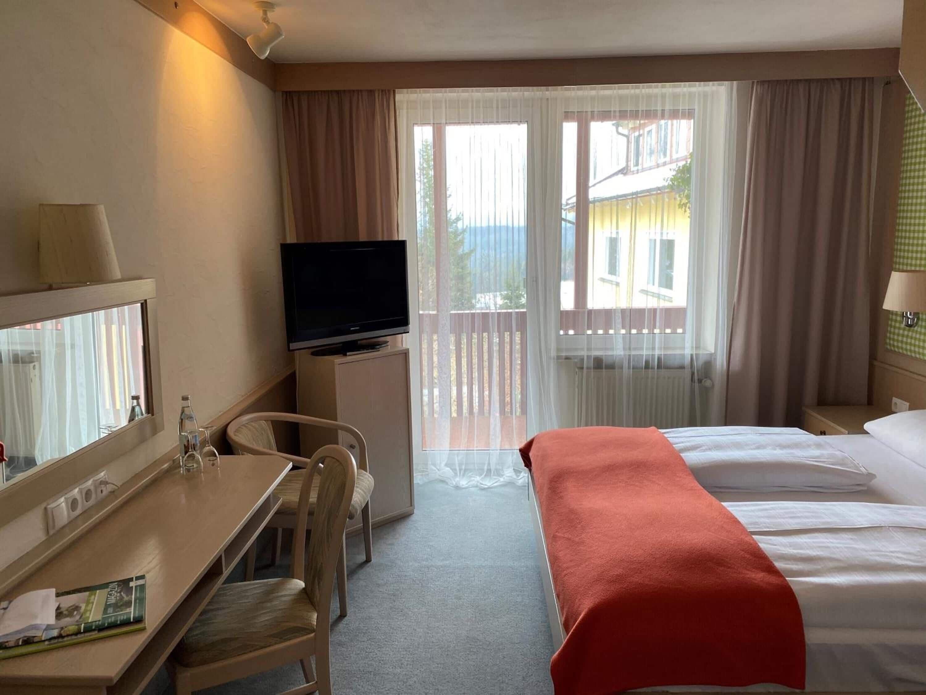 Habitación de hotel con cama, escritorio y silla, televisor y ventana con cortinas.