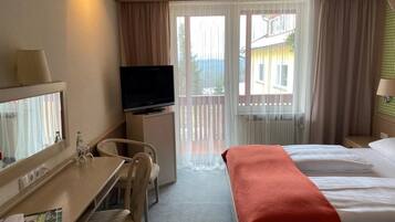 Habitación de hotel con cama, escritorio y silla, televisor y ventana con cortinas.