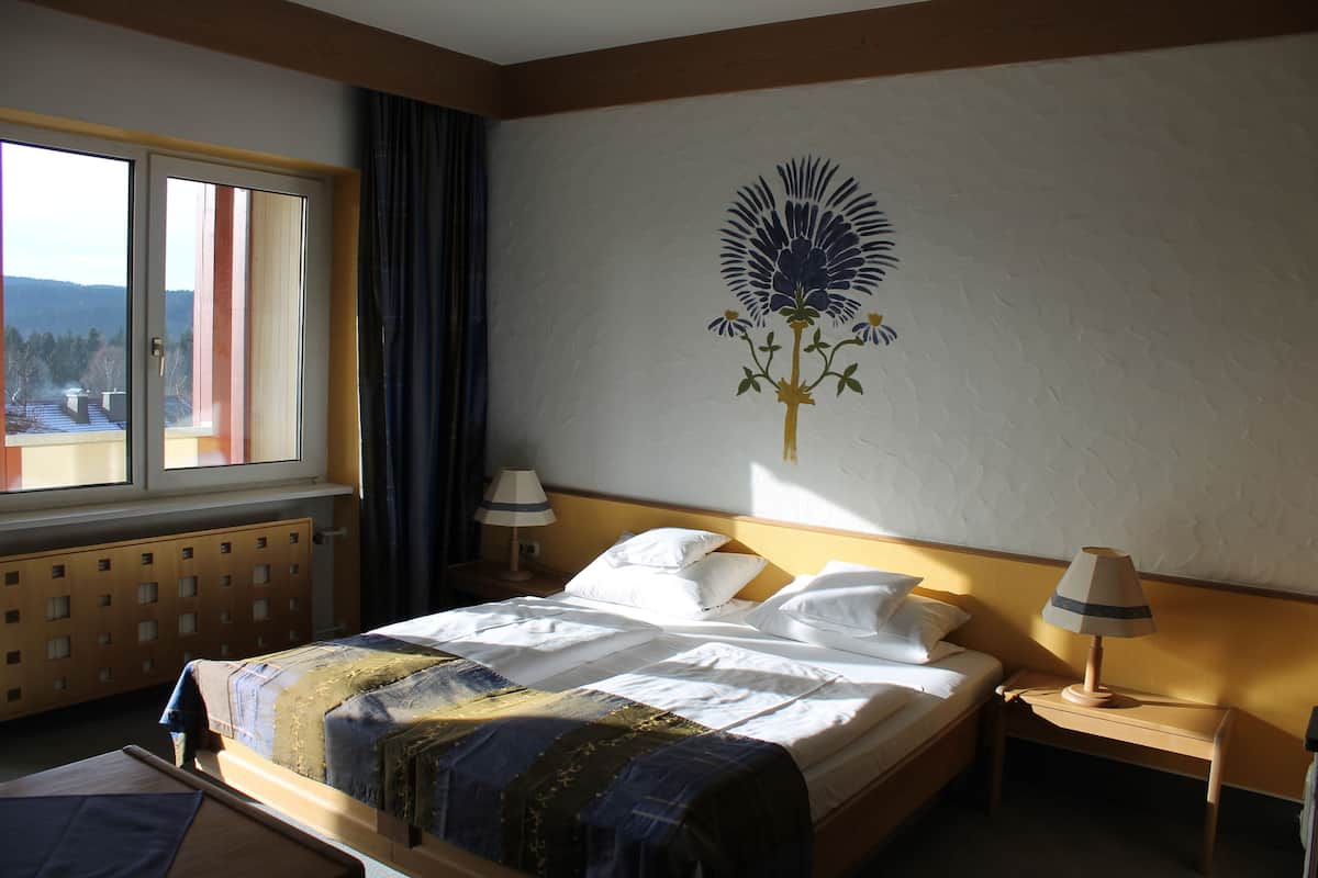 Une chambre d’hôtel comprenant un lit, deux tables de chevet, une fenêtre avec des rideaux et un élément décoratif mural.