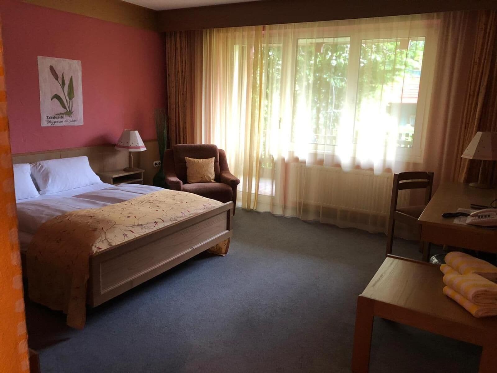 A hotel room with a bed, a chair, a desk, a lamp, and a window with curtains.