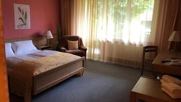 A hotel room with a bed, a chair, a desk, a lamp, and a window with curtains.