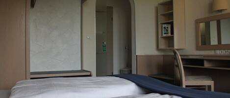 Una habitación de hotel con una cama, un escritorio, una silla y un armario.