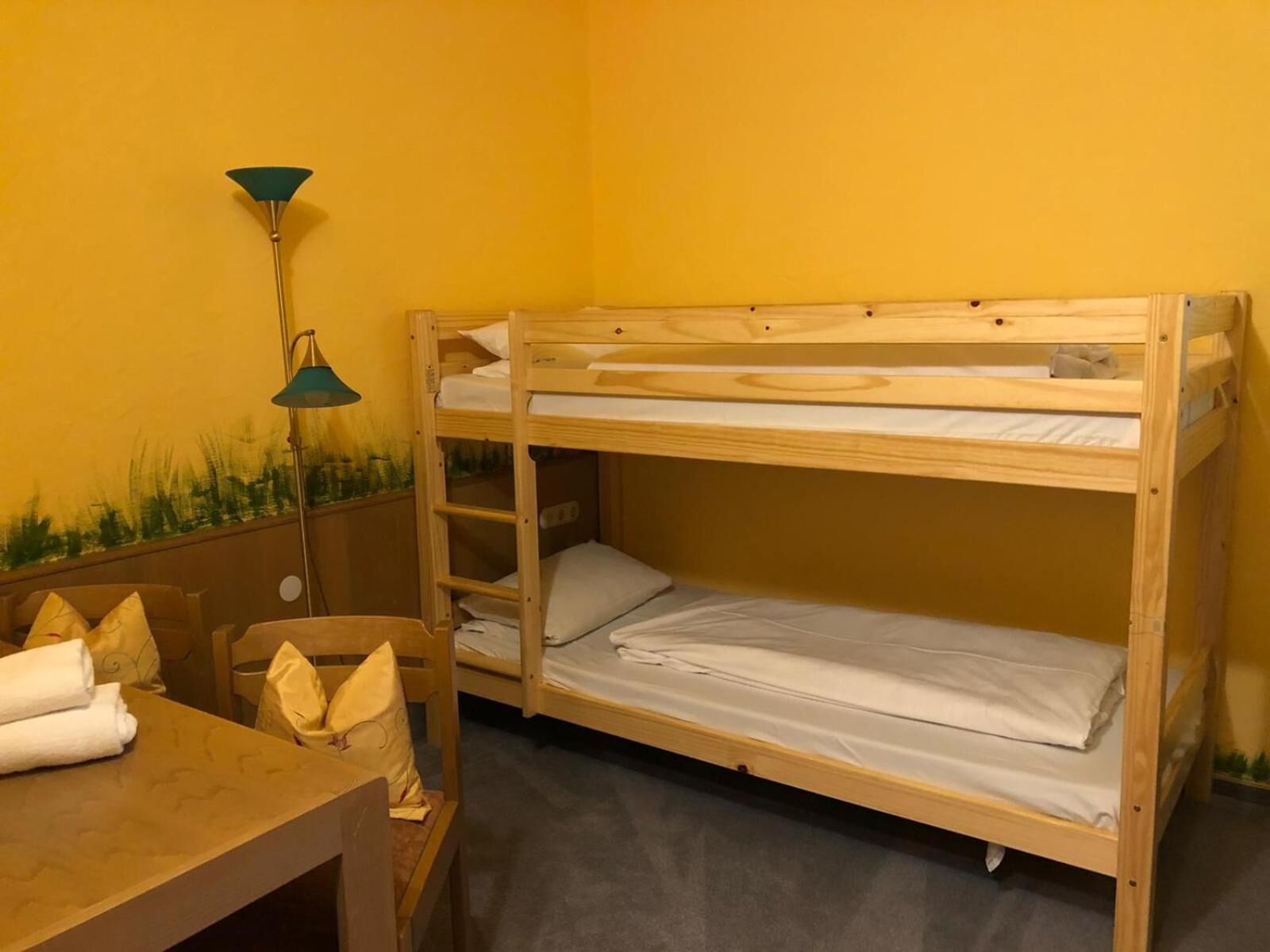 A bunk bed room with a wooden table and chairs, a lamp, and a wall mural.