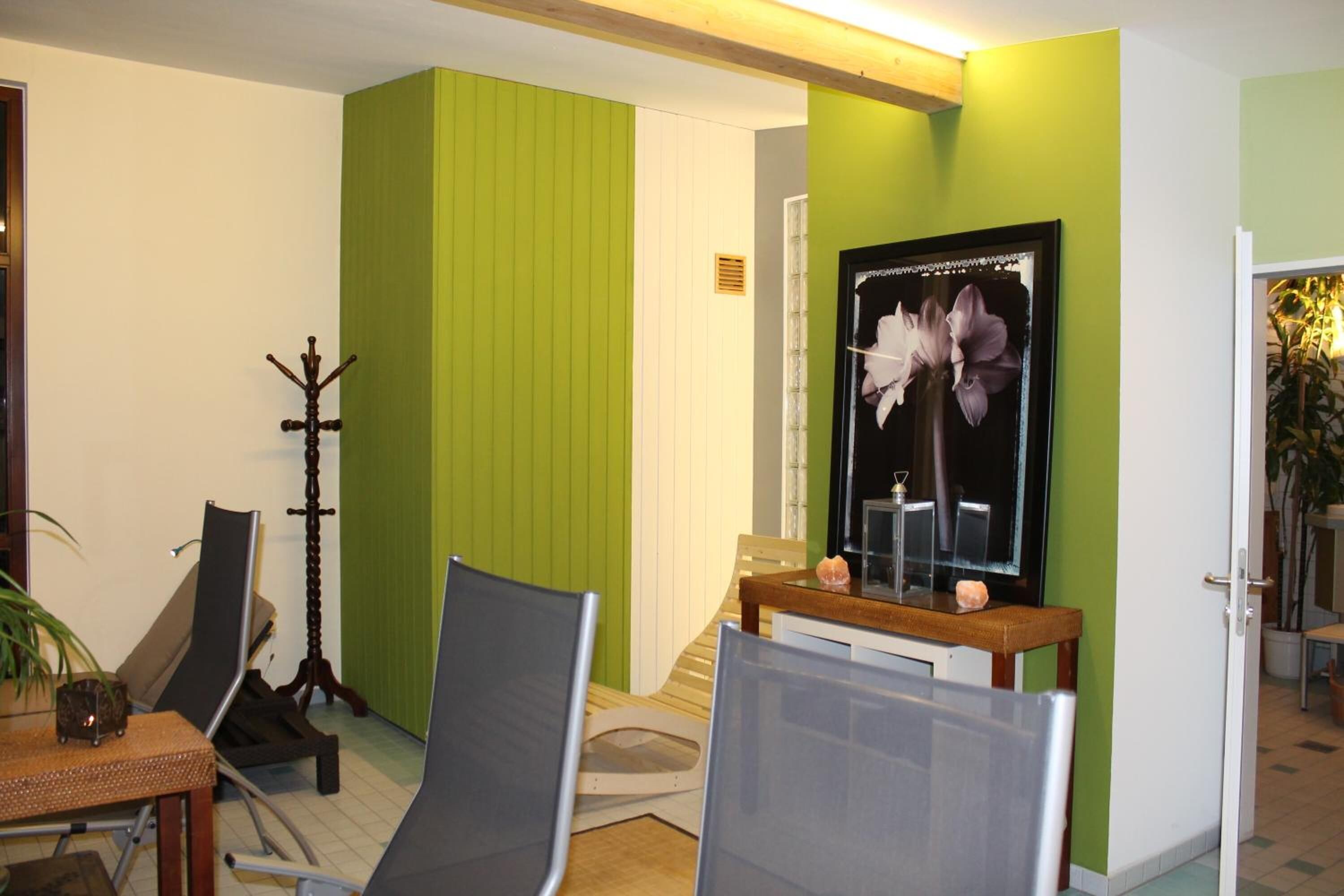 Ein Zimmer mit grüner Akzentwand, einem Holz-Kleiderhaken, einem Spiegel mit floralem Muster und einem kleinen Tisch mit Kerze.
