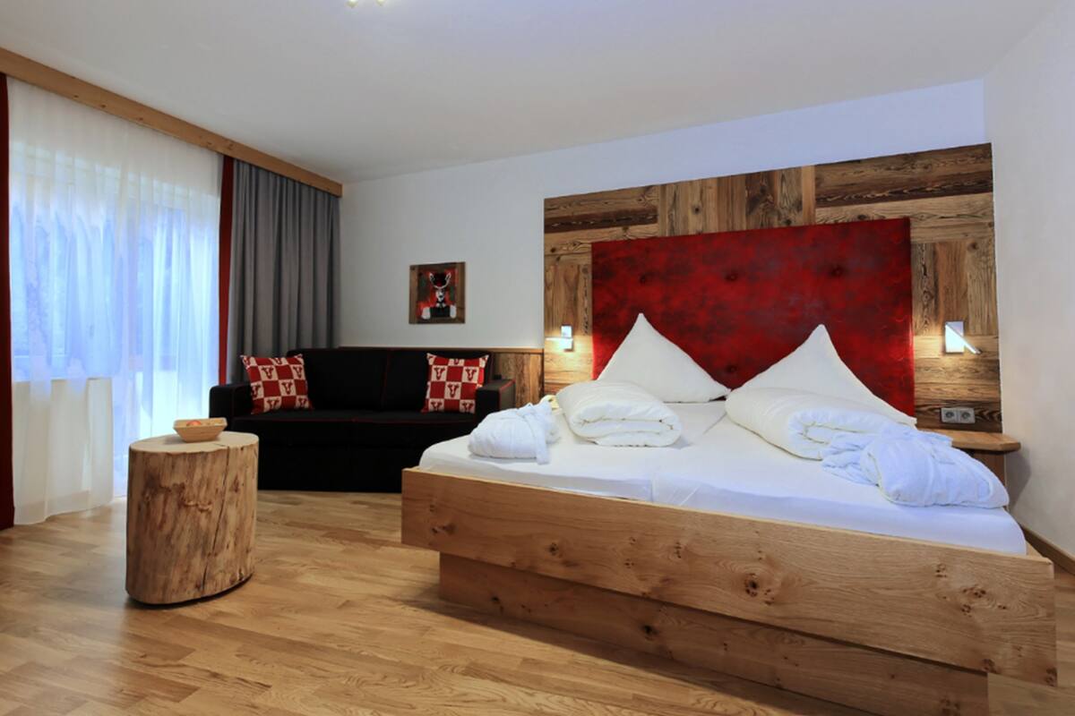 Een moderne slaapkamer met een houten bed, een donkere bank en een ronde houten tafel.