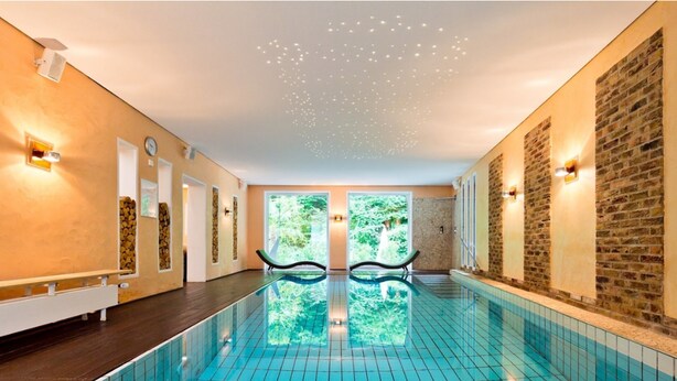 Ein großes Hallenbad mit klaren blauen Fliesen, einer Holzterrasse und einer Steinwand.