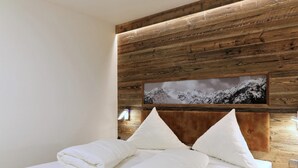 Ein ordentlich bezogenes Bett mit weißen Leinen und Kissen, ein hölzernes Kopfteil und ein gerahmtes Bild einer verschneiten Berglandschaft.