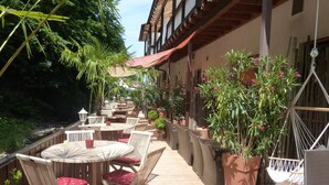 Eine Außenpatio-Terrasse mit runden Tischen und Stühlen, umgeben von Topfpflanzen und einem Hängesessel.