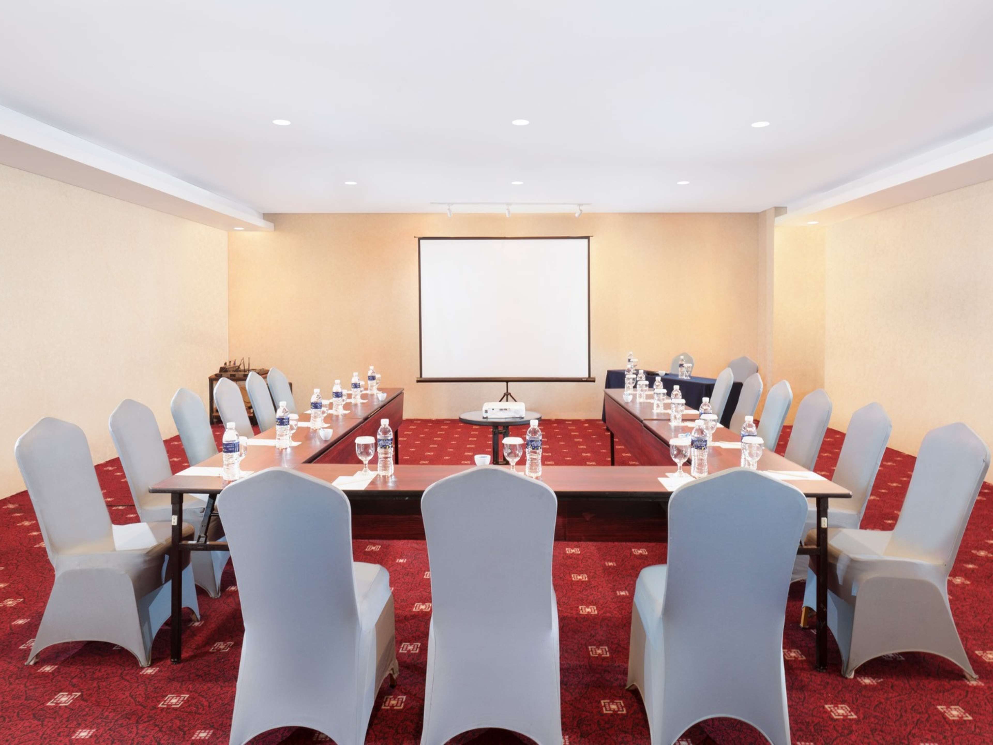 A conference room with a long table, chairs, a projector screen, and water bottles.