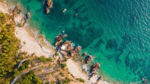 Vue aérienne d’une zone côtière avec des eaux turquoise limpides, des affleurements rocheux et une plage de sable.