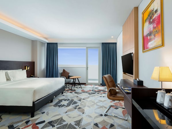 Habitación de hotel con cama, escritorio con silla, televisor y una ventana grande con cortinas.