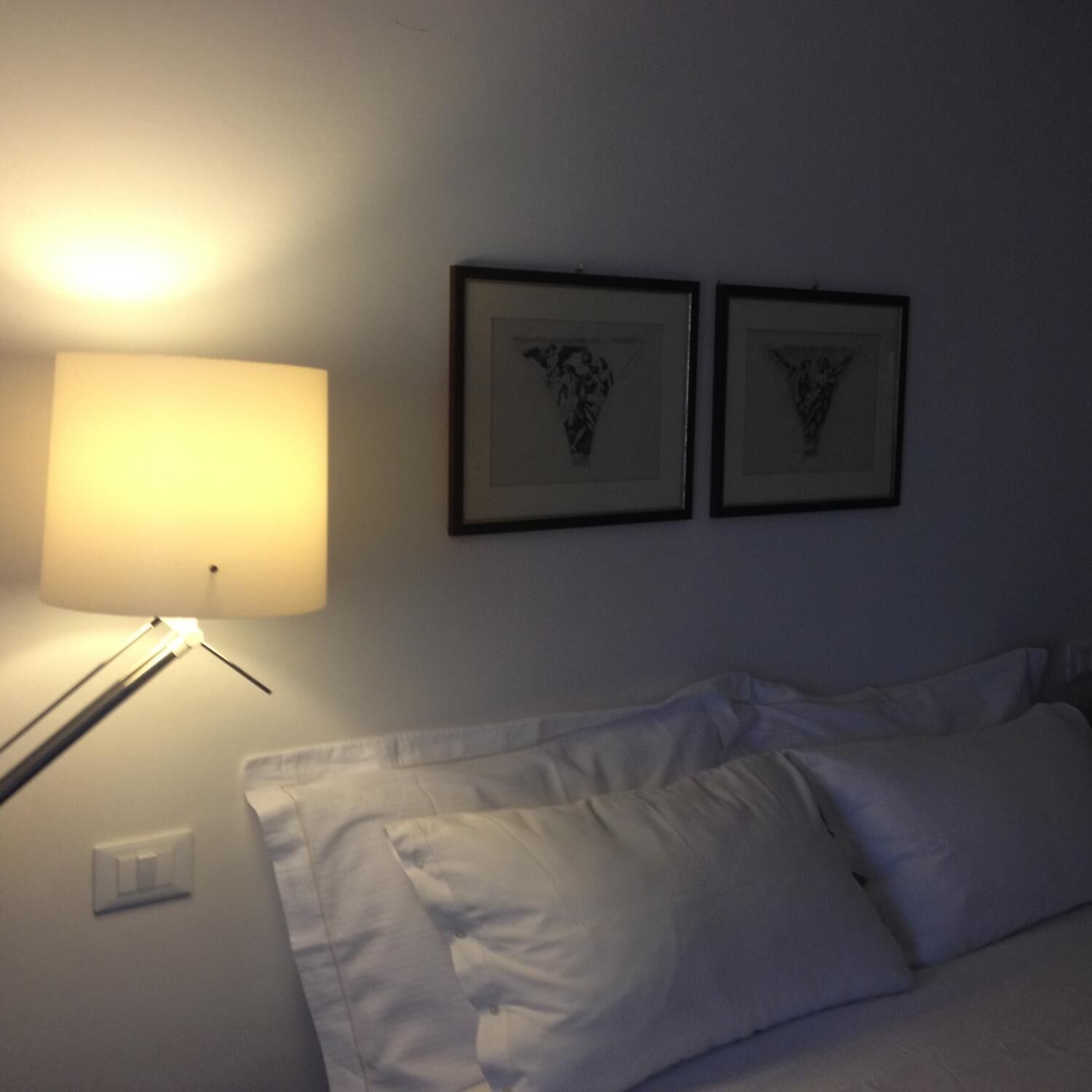 A hotel room with a bed, a bedside lamp, and two framed pictures on the wall.