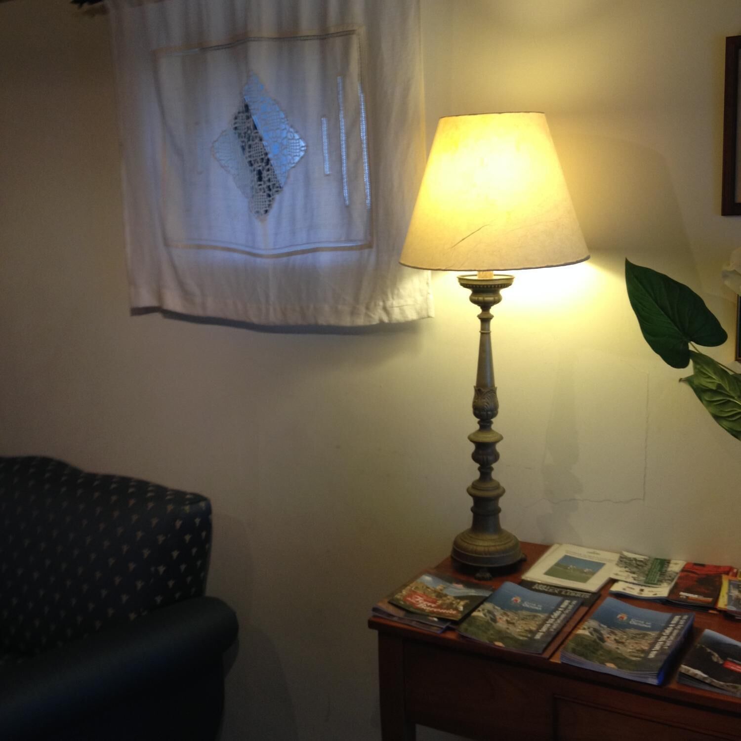 Ein Zimmer mit einer Tischlampe, einem Sessel und einem Fenster mit Spitzenvorhang.