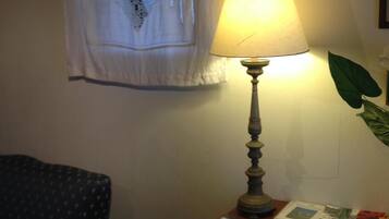 Ein Zimmer mit einer Tischlampe, einem Sessel und einem Fenster mit Spitzenvorhang.