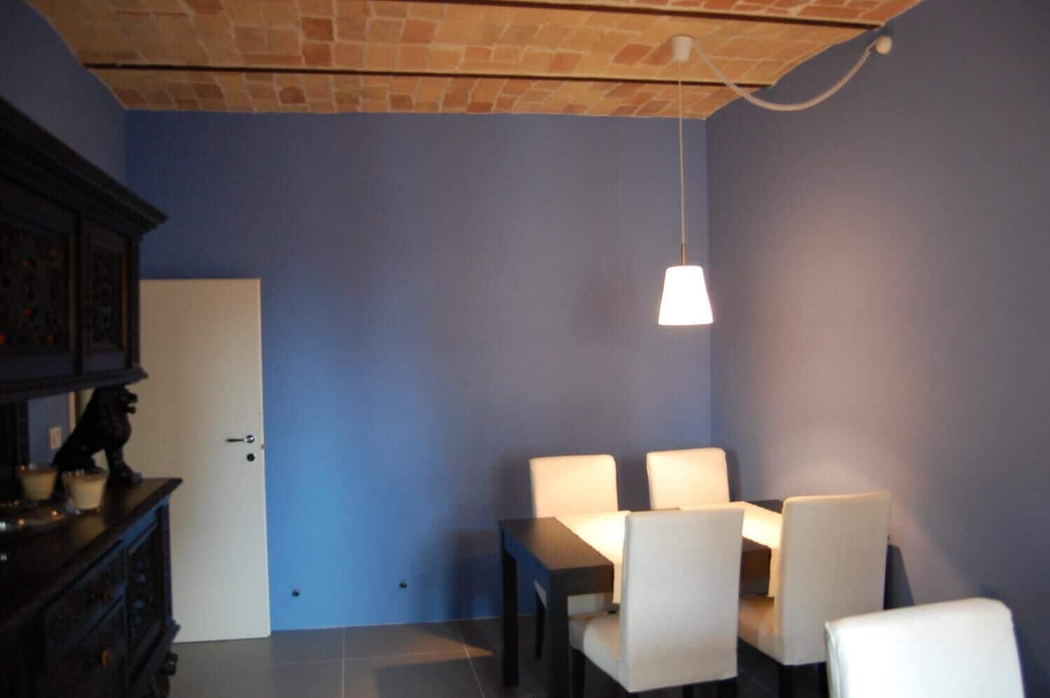 A dining area with a table and chairs, a hanging light fixture, a door, and a dark wooden cabinet.