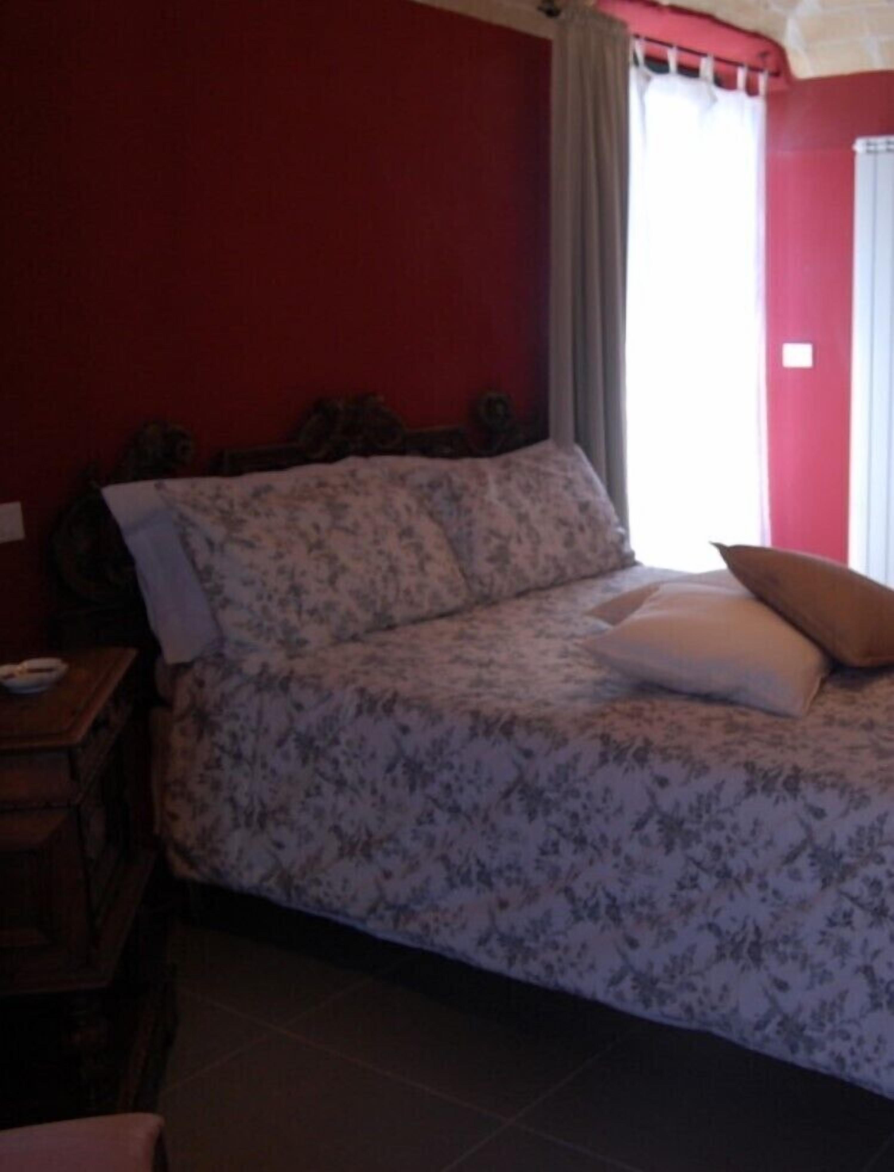 A bedroom with a floral bedspread, a wooden nightstand, and a window with curtains.