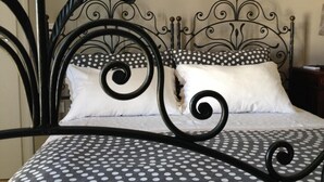 Una cama con estructura metálica negra, ropa de cama blanca y negra con lunares y dos almohadas con diseños de lunares y blanco liso.