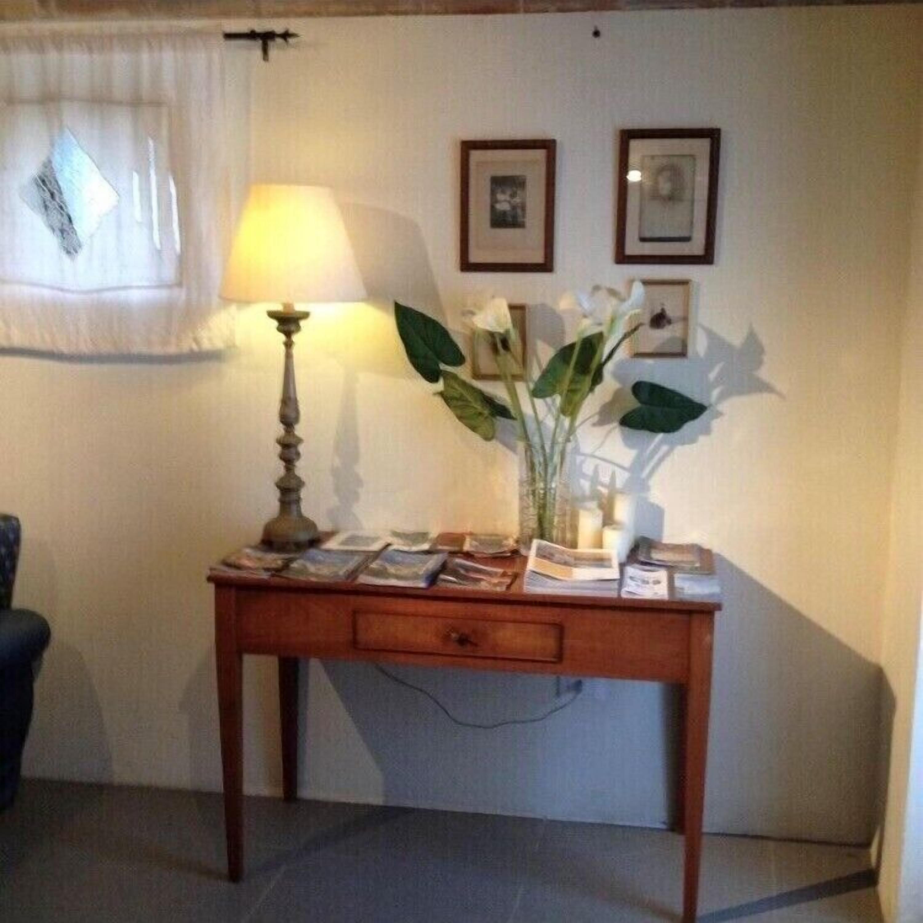 Un escritorio de madera con una lámpara, un florero con flores y cuadros en la pared.