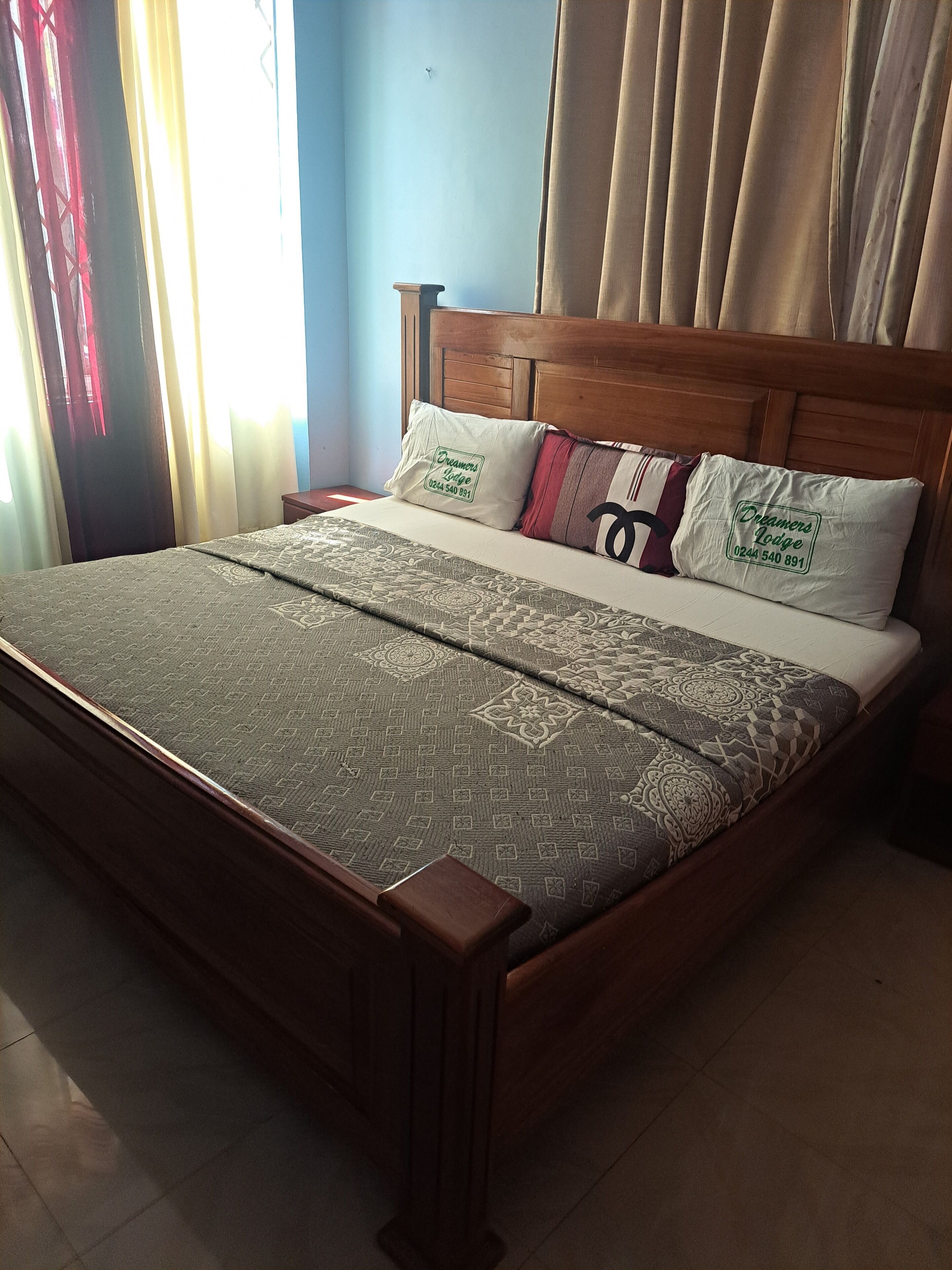 Ein Bett mit gemustertem Überwurf, Holz-Kopfteil und zwei Kissen mit einem Logo.
