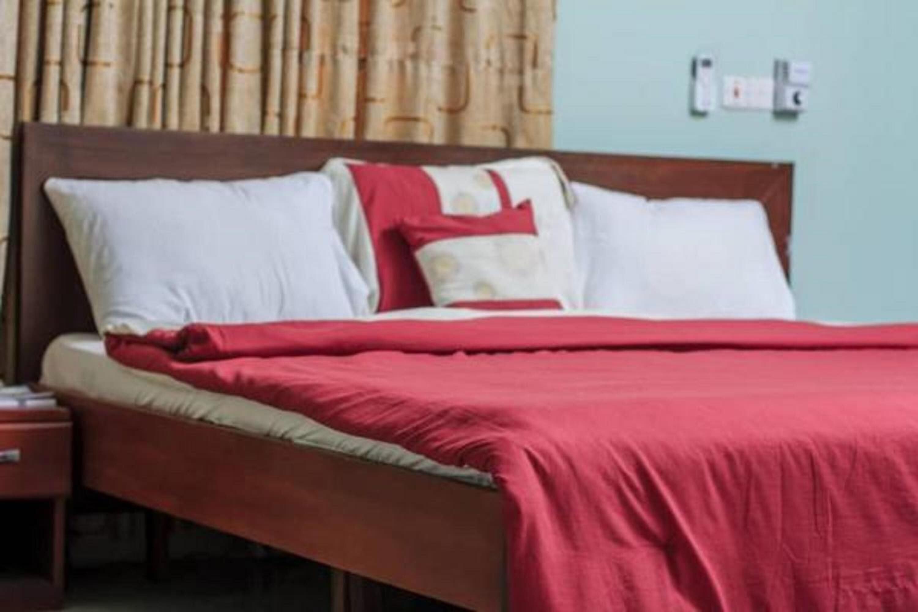 A bed with a red blanket, white pillows, and a wooden headboard.