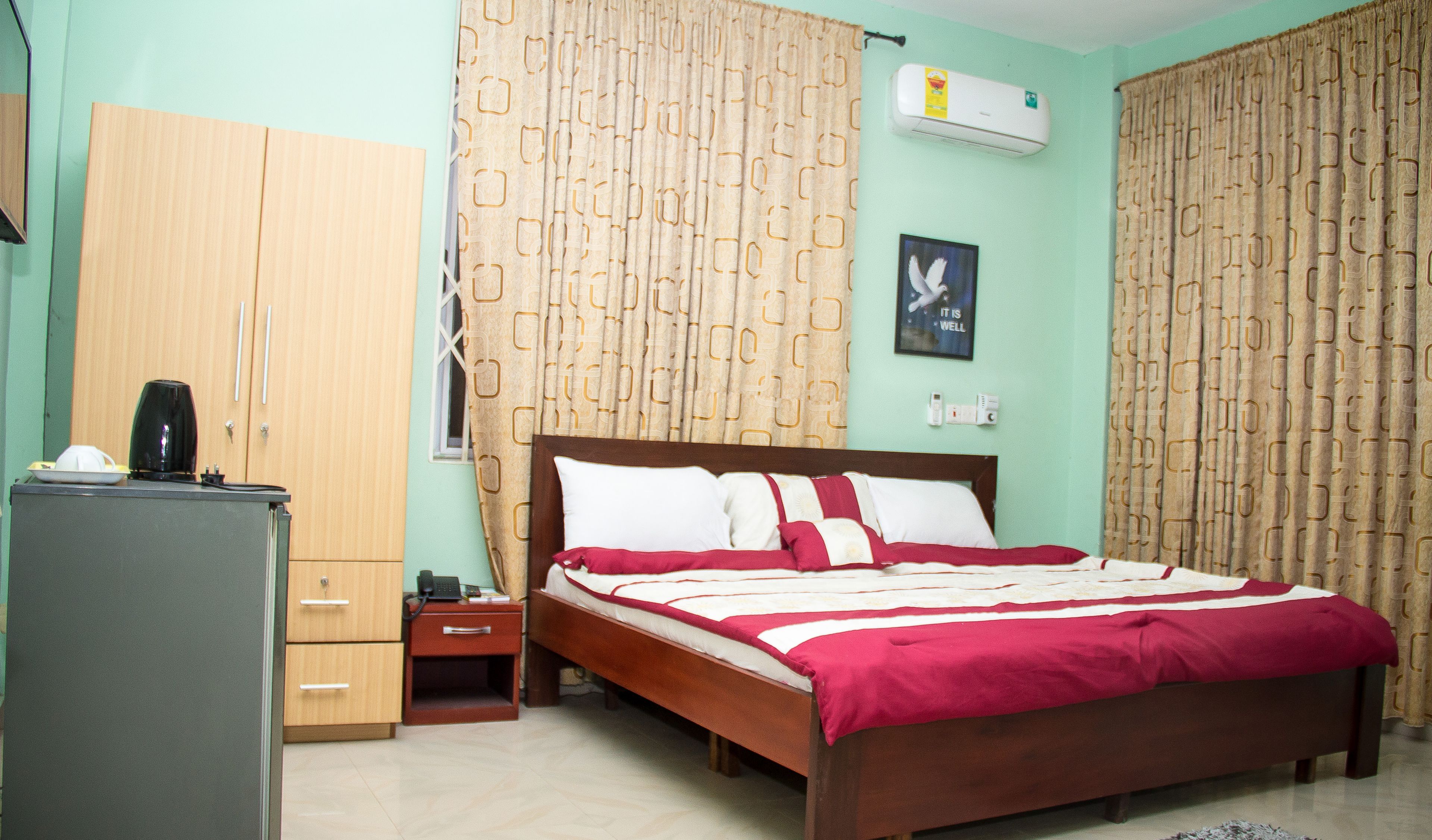 A bedroom with a bed, a wardrobe, a desk with a lamp, and an air conditioner.