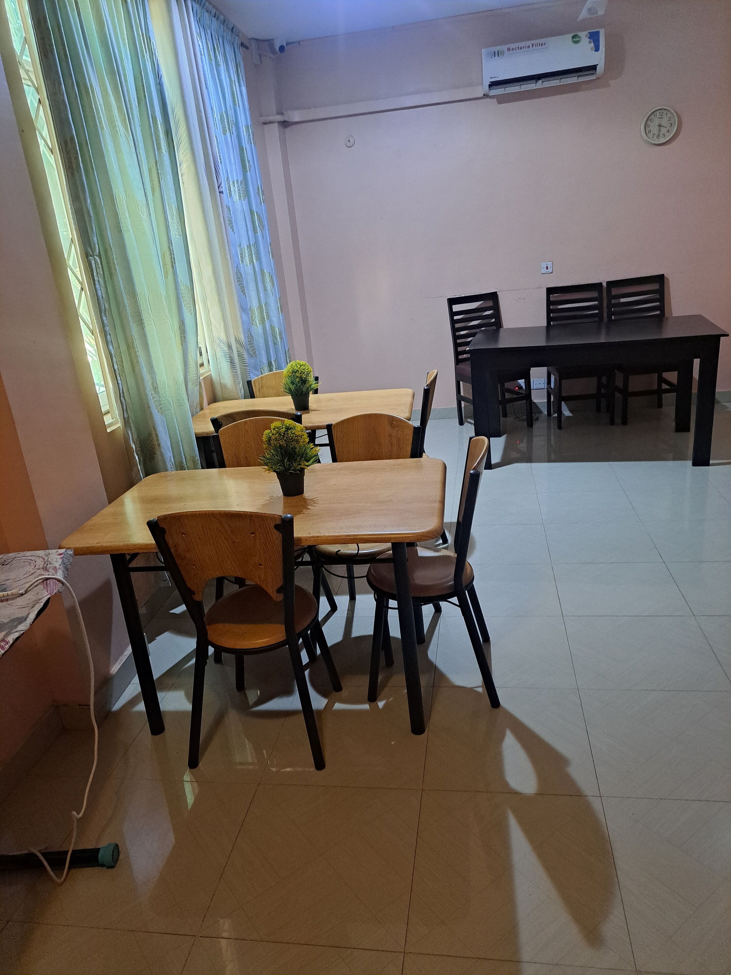 A dining area with wooden tables and chairs, a clock on the wall, and an air conditioning unit.