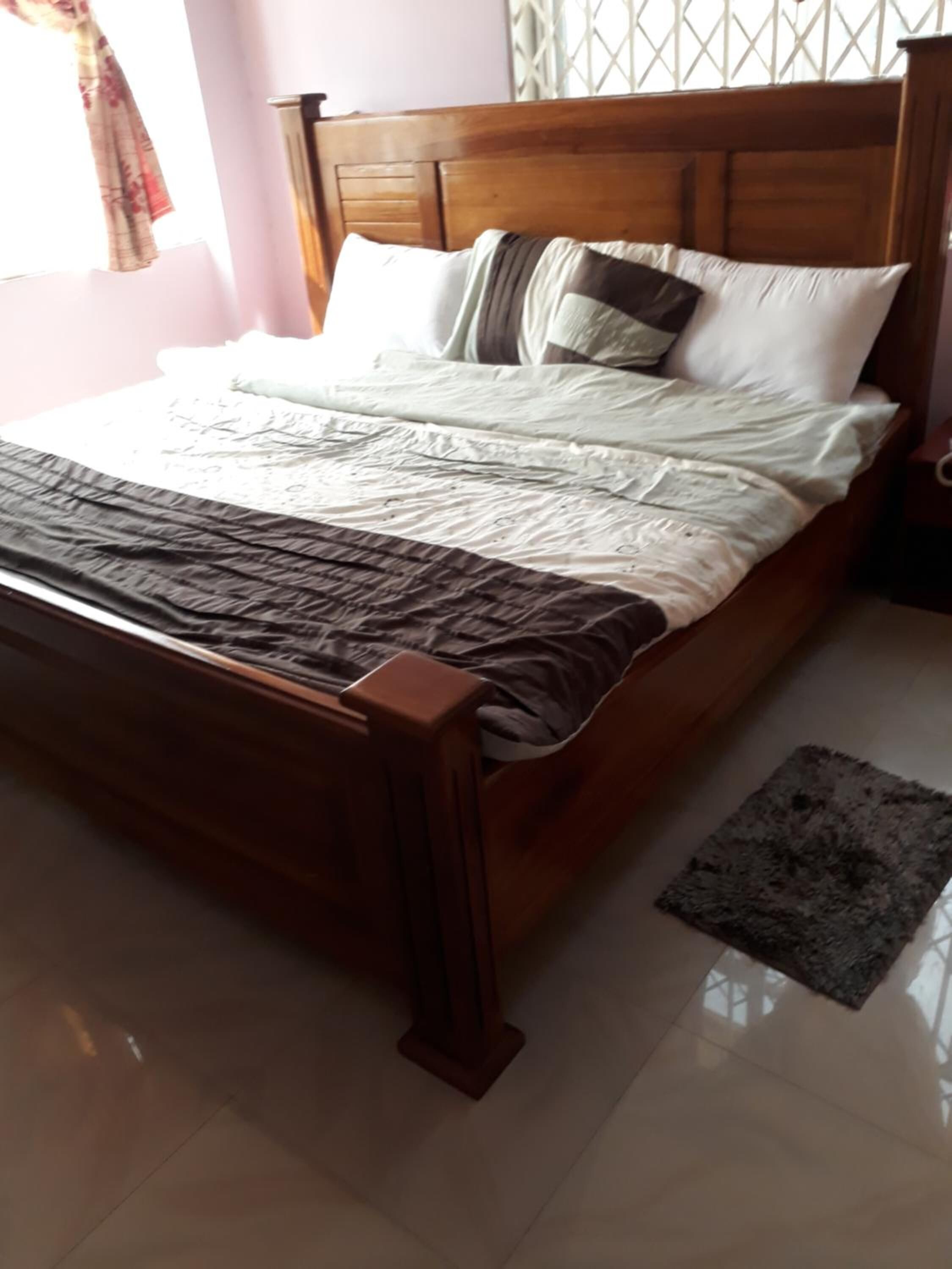 Una cama con estructura de madera, ropa blanca de cama y una manta de color marrón oscuro.